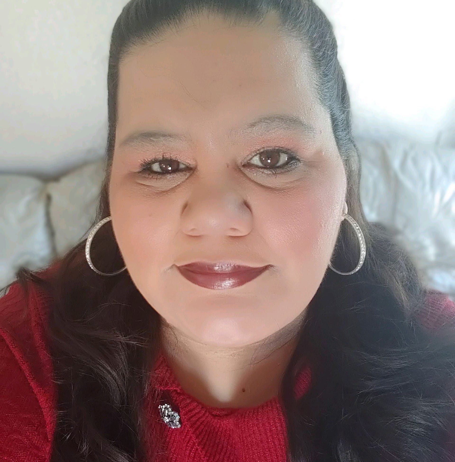 A selfie of a woman wearing a vibrant red blouse and full makeup