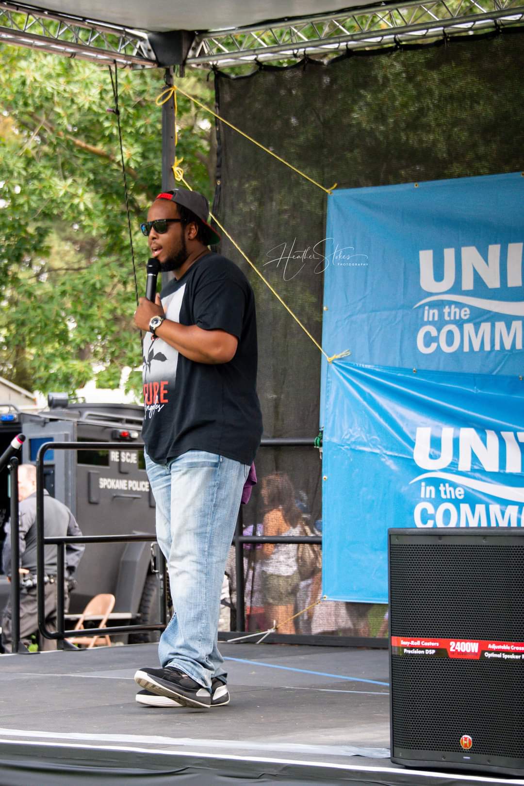 A confident man stands on a stage, holding a microphone while speaking to an audience