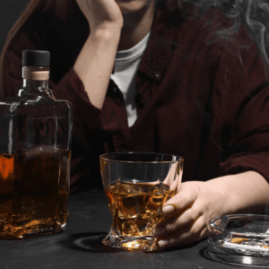 Alcohol addiction photo of a woman with whiskey and smoldering cigarettes