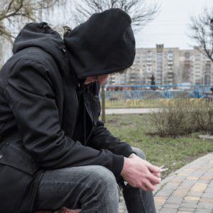 Man sitting on a bench wearing a black jacket in hood featuring substance abstinence