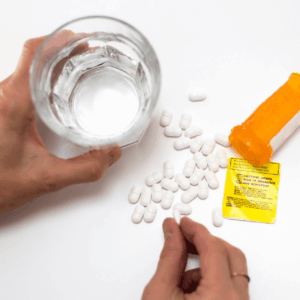 Opioid use disorder, opioid pills, pill bottle, woman's hands on glass of water. Overhead shot in white background.